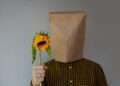a person with a paper bag on their head holding a sunflower